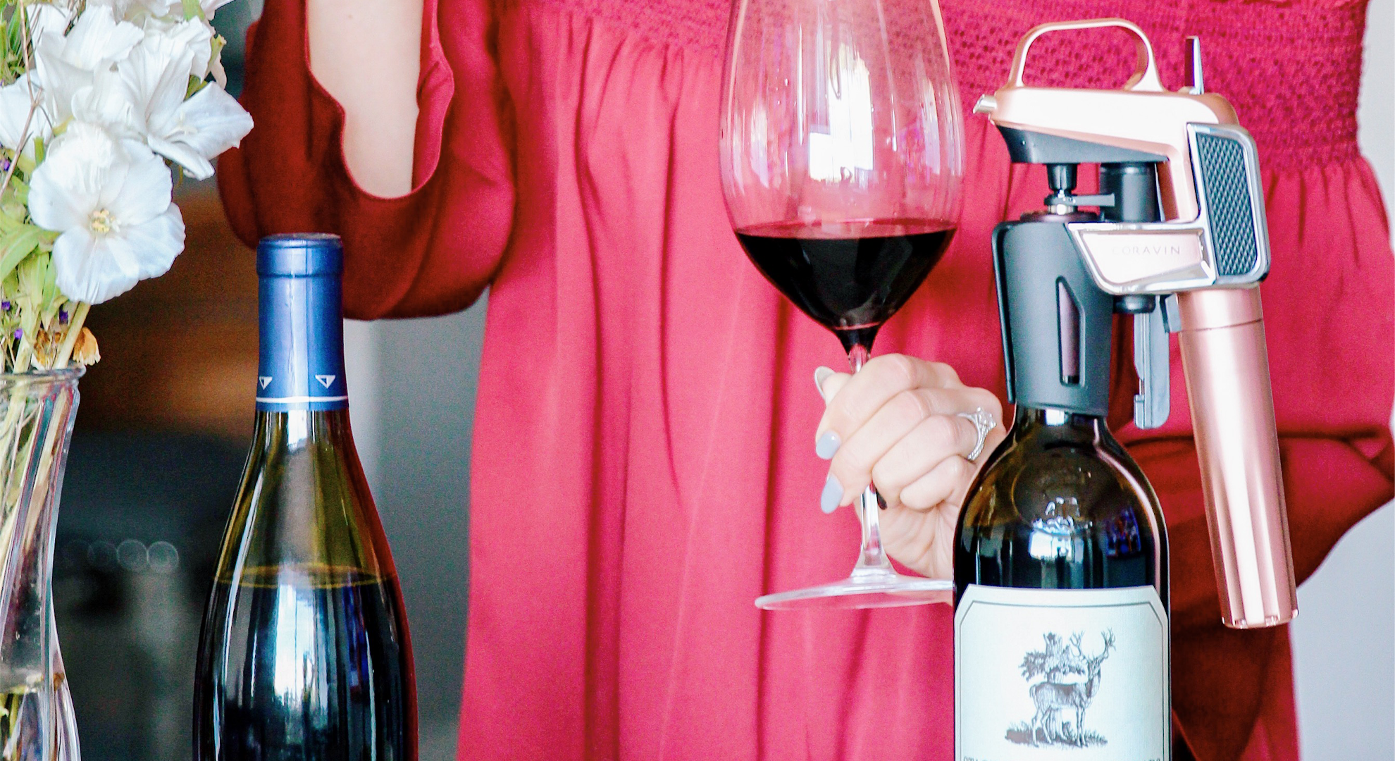 Woman holding a glass of red wine featuring a Coravin Wine Preservation System on bottle.